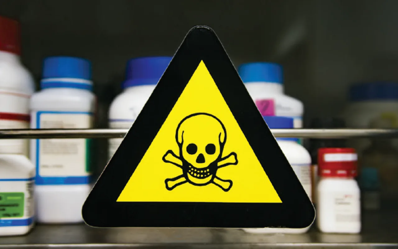 skull and cross bones warning label in front of a shelf of bottles